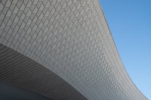 A close cropped detail of the Maat ceiling. the ceiling is in a flowing curved form and covered in small tiles. A cloudless sky can be seen behind.